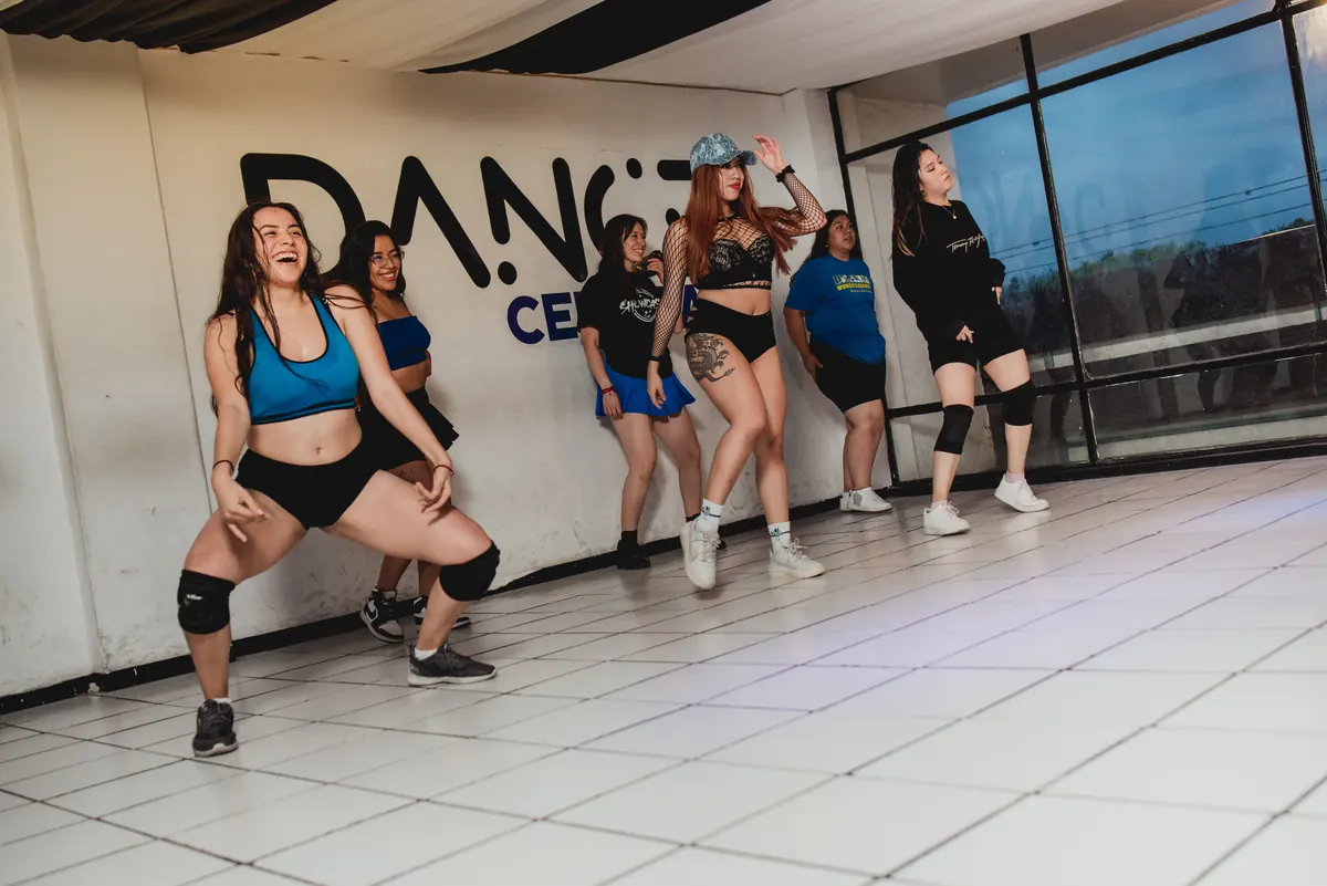 Bailarinas de Dance Central marcando un paso de baile moderno frente al logotipo del estudio
