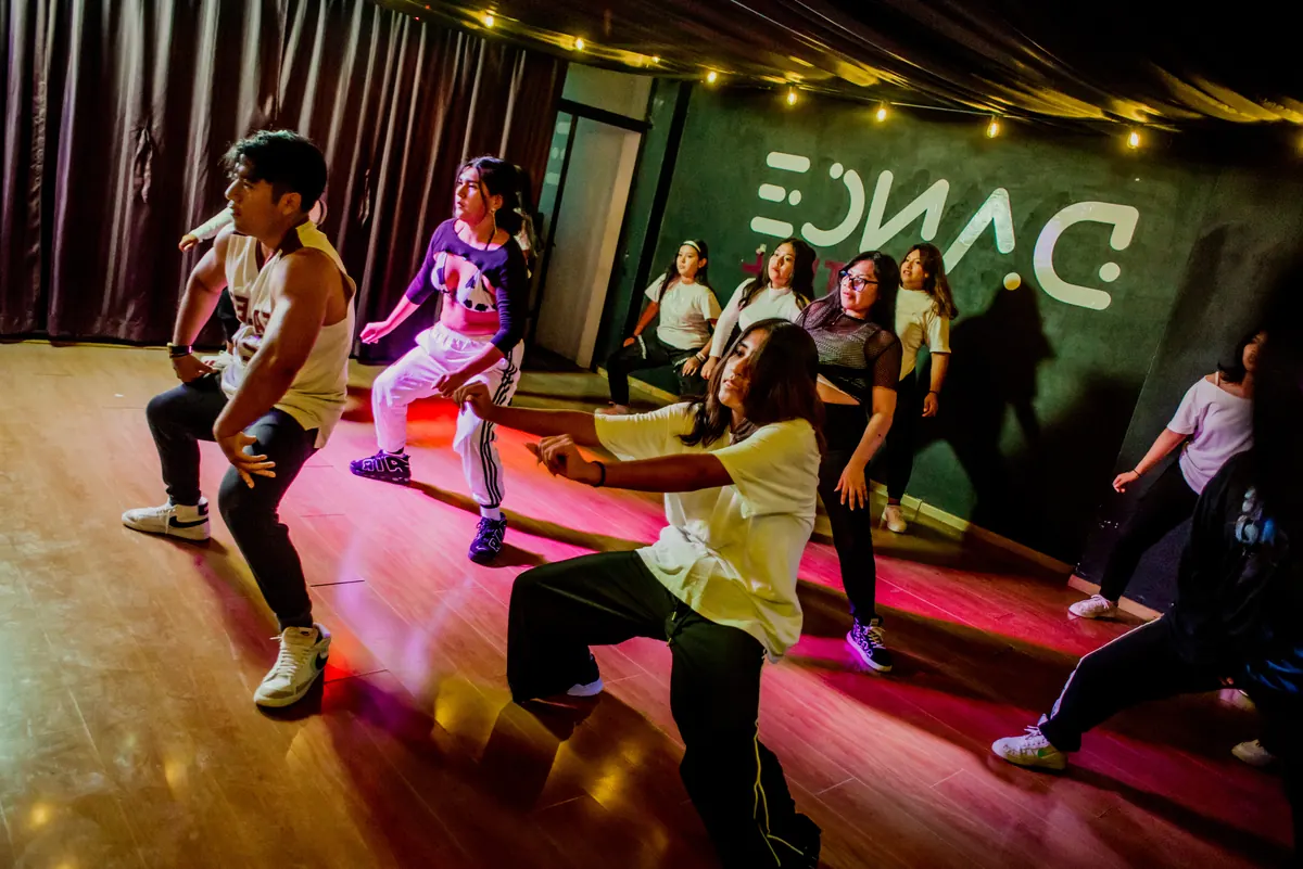 Grupo mixto de la clase de hip hop de Dance Central bailando bajo luces rosas, con el logotipo del estudio al fondo
