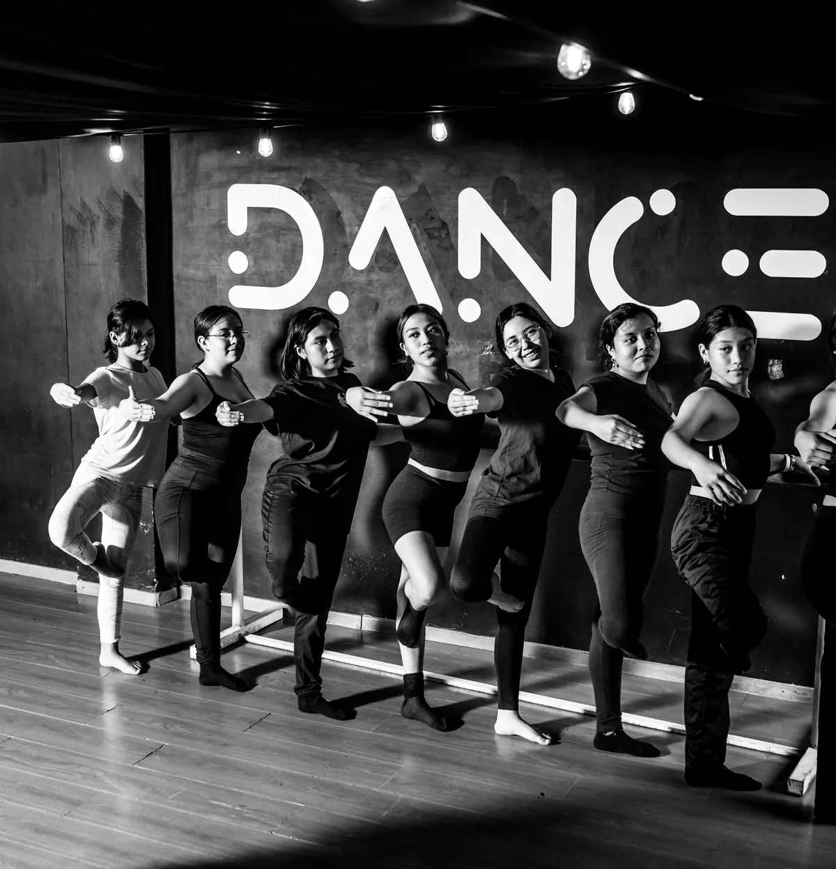 Alumnas de Dance Central alineadas en la barra durante una clase, frente al logotipo pintado en la pared del salón